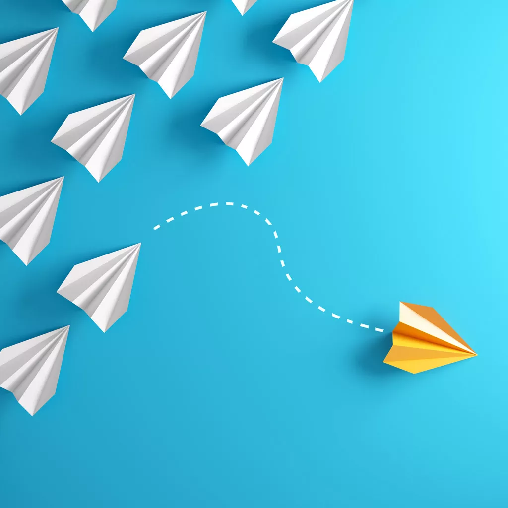 Plusieurs avions en papier blanc et une avion en papier jaune qui se démarque.