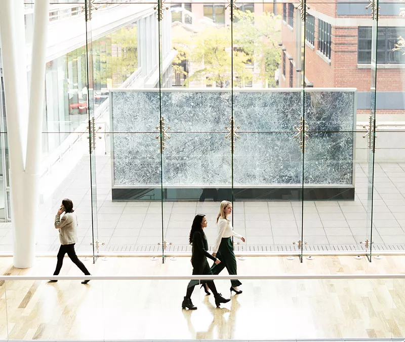 Personnes qui marchent sur le Parquet dans l'Édifice Jacques-Parizeau, avec une vue sur l'exétieur..